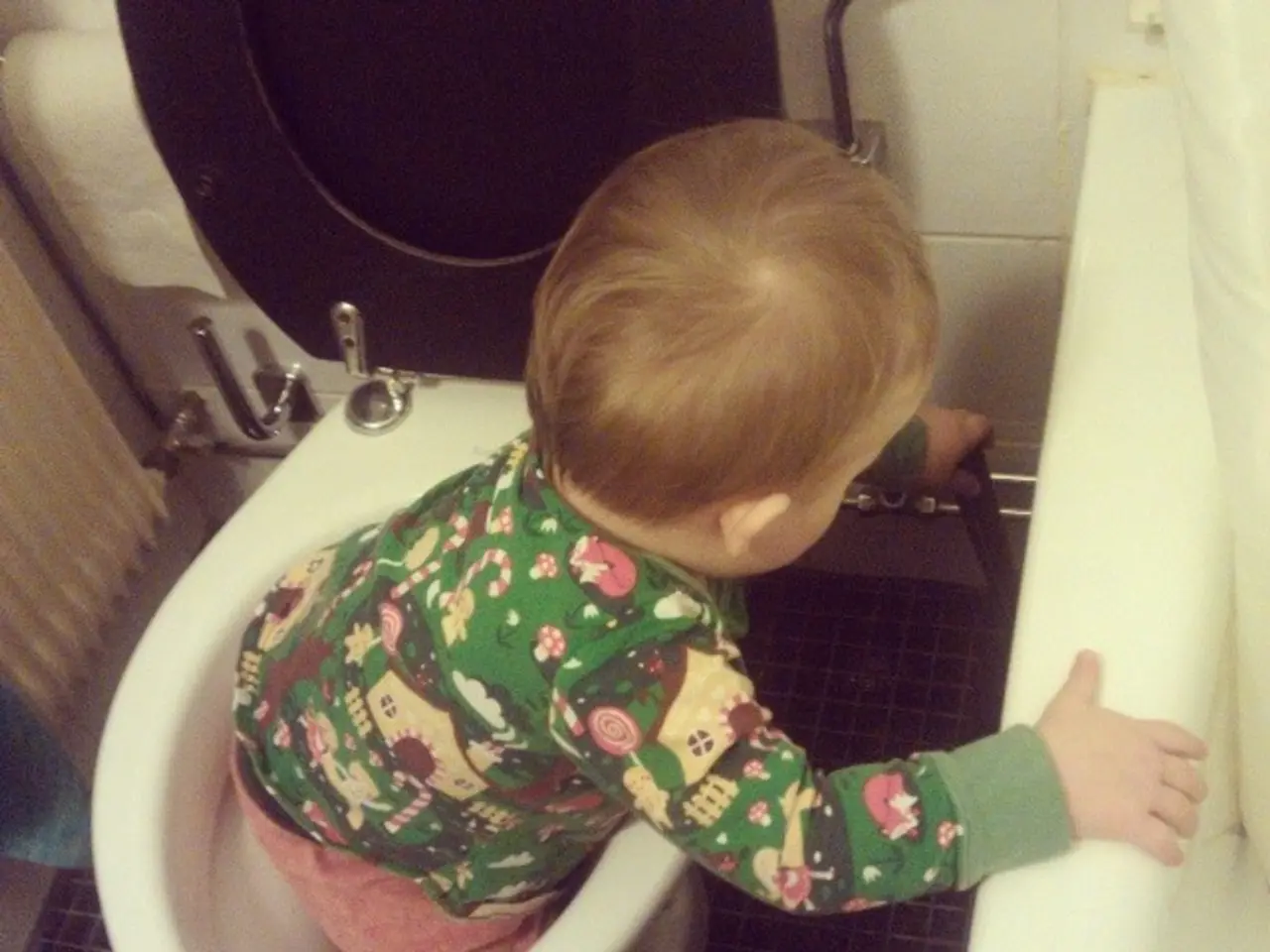 In the image a kid is standing in a western toilet. Behind the western toilet there is wall.