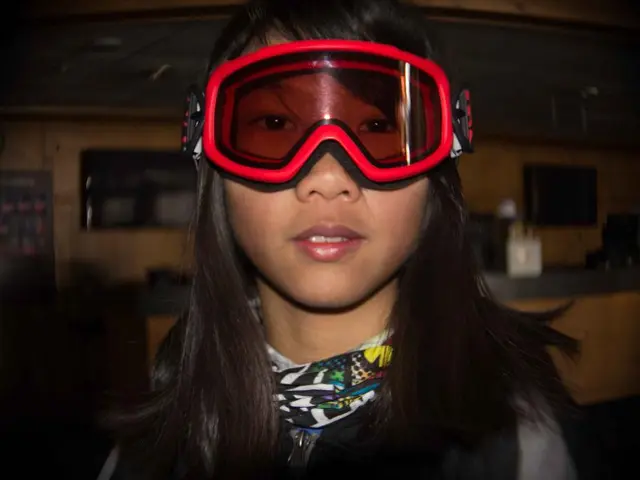 In this image I can see a girl wore red color goggles. She wore scarf around her neck behind her...