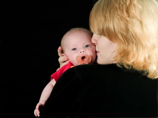 In this image, we can see a woman in black dress is holding a baby. Background we can see the dark...