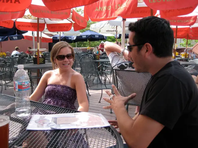 An outdoor picture. This are umbrellas. Far there are trees. This are chairs and tables. On this...