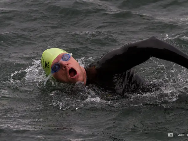 In this image there is a man swimming in the water. He wore the cap and the goggles and swimming in...